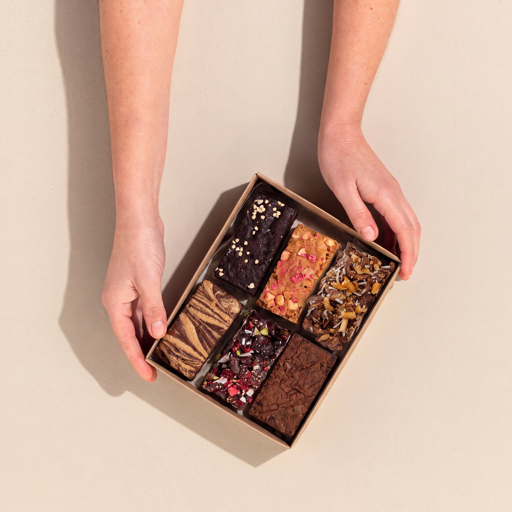Individual brownie and rocky road pieces to form the mini sample pack, being held by hands