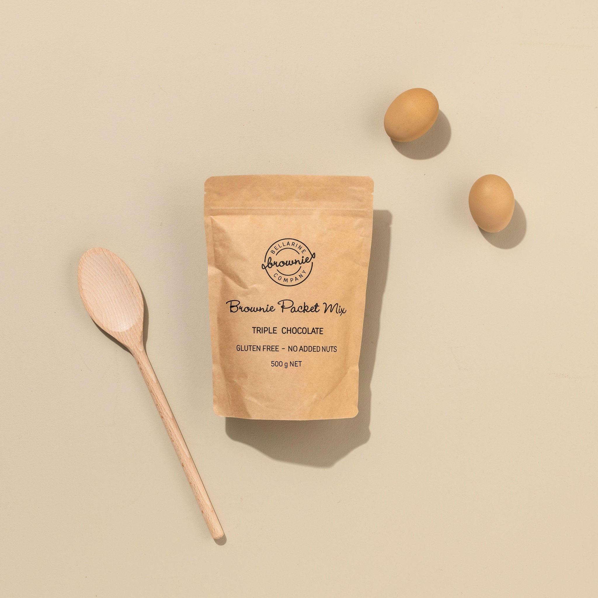 Brownie packet mix packaging with a wooden spoon and eggs on a beige background