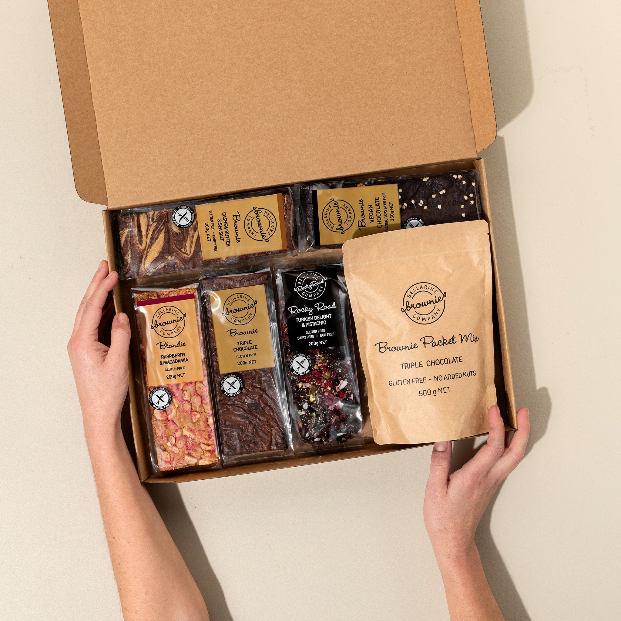 Open box of assorted brownie and rocky road bars held by hands on a beige background