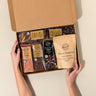 Open box of assorted brownie and rocky road bars held by hands on a beige background